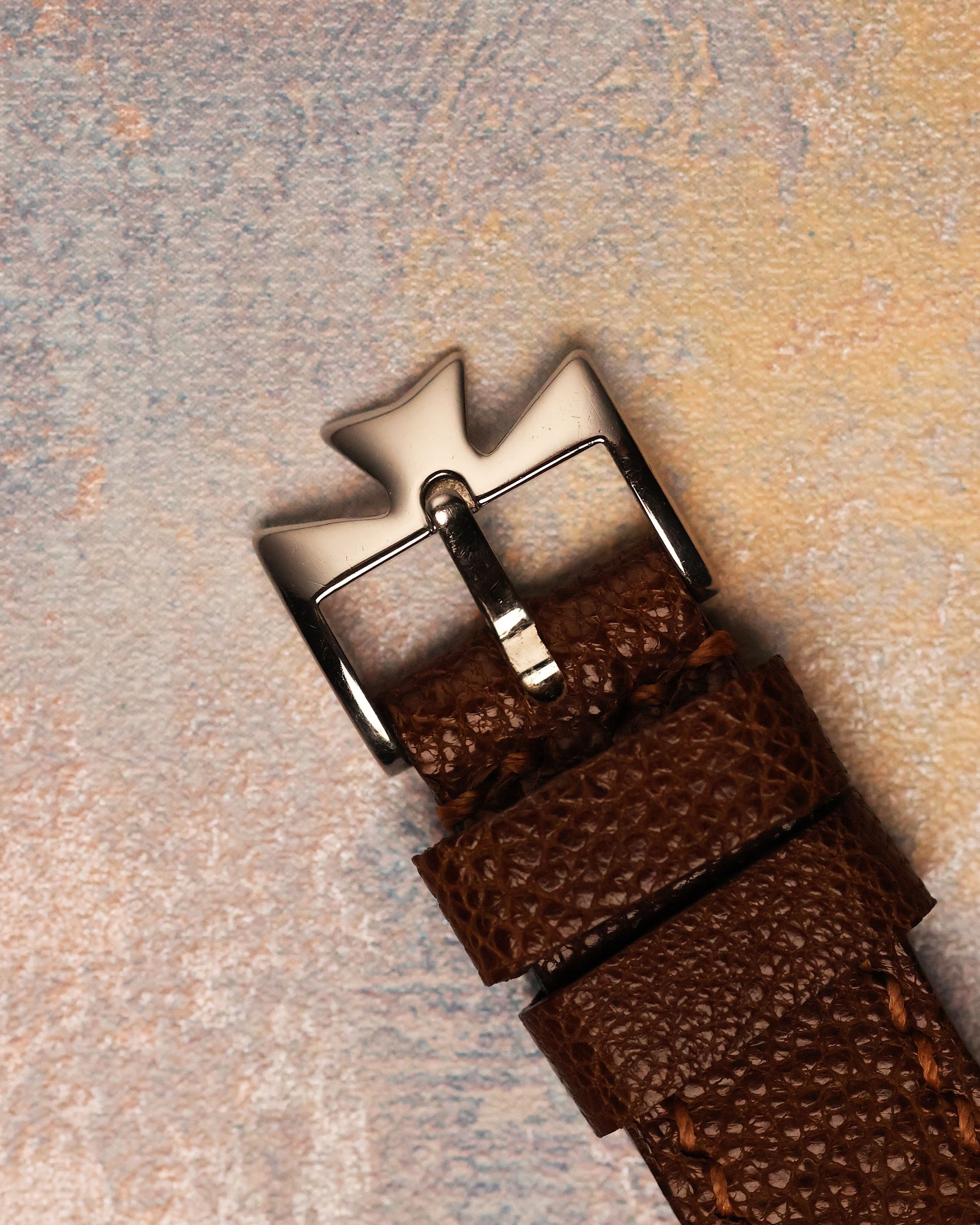Vacheron Constantin platinum Maltese cross buckle on brown textured leather strap, emphasizing craftsmanship and design continuity.