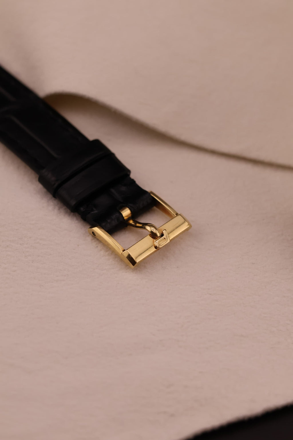 Close-up of original Piaget gold buckle from the top, attached to the black leather strap.