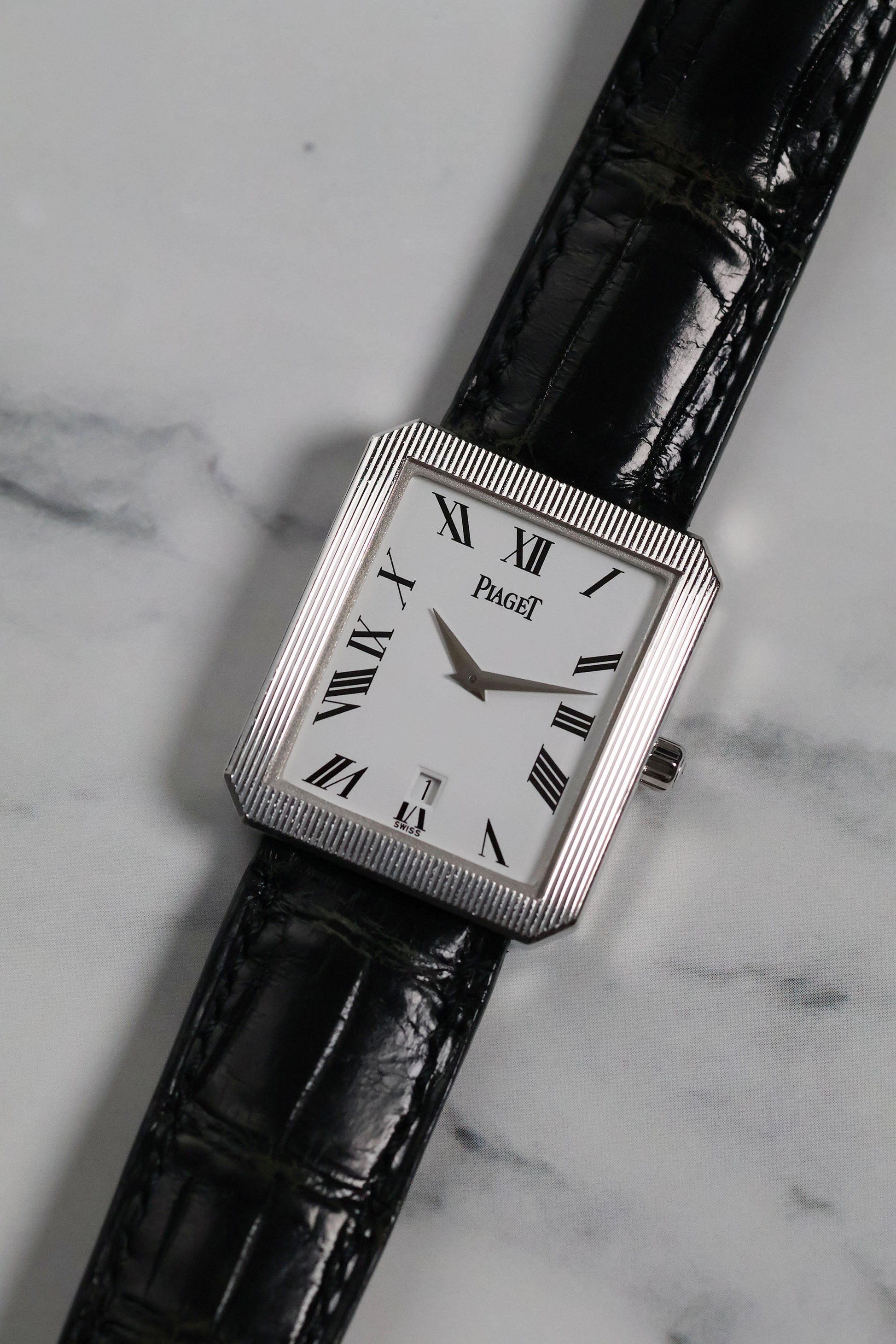 Frontal view of Piaget Ref. 26354 in 18K white gold with fluted bezel and Roman numeral dial on black leather strap.