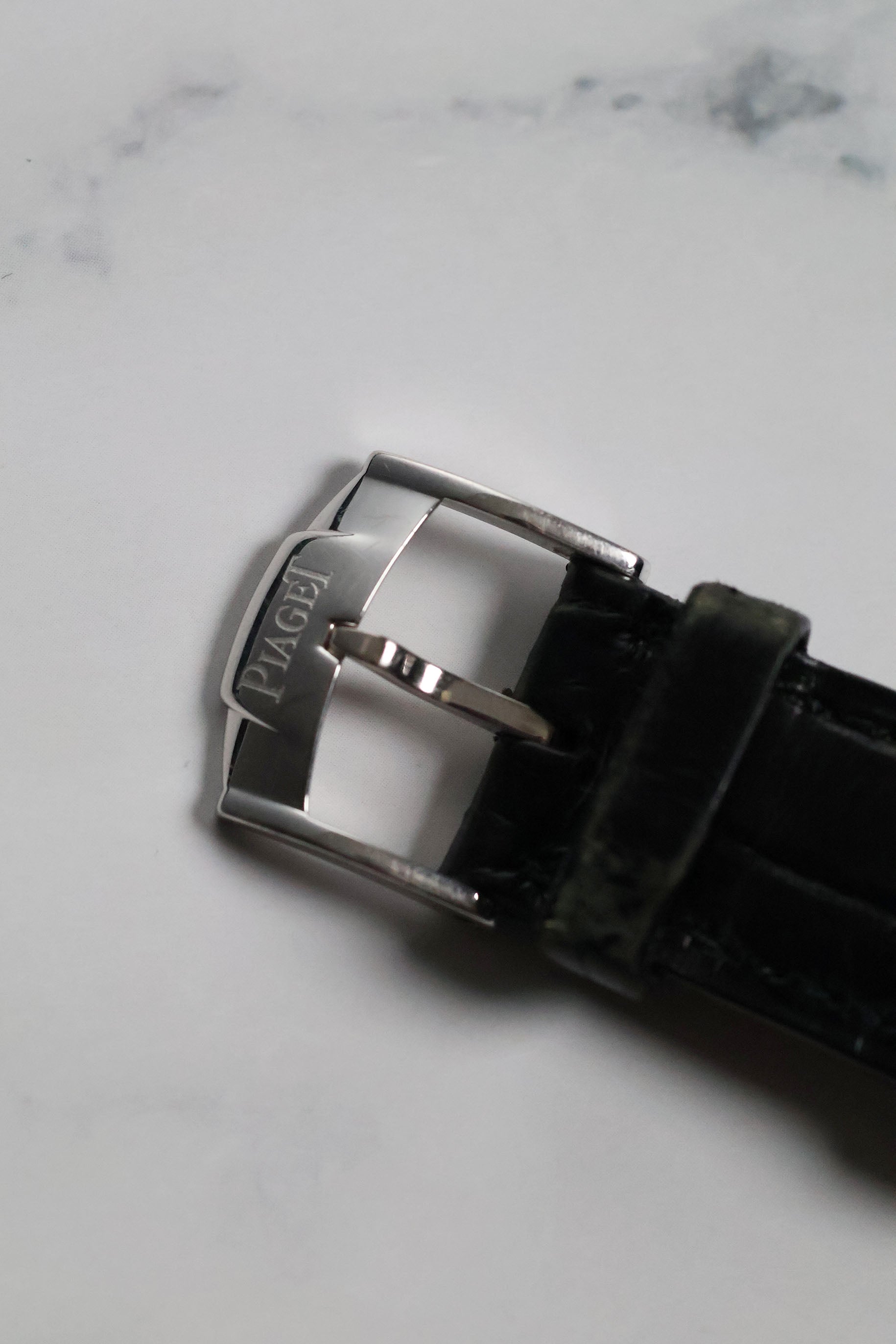 Top view of original Piaget-signed 18K white gold buckle attached to black leather strap.