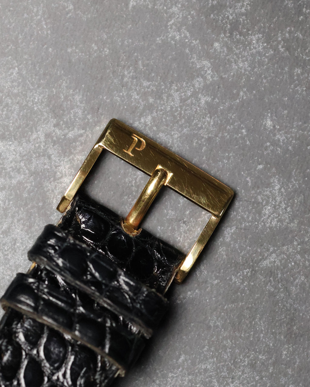 Original 18K yellow gold Piaget buckle viewed from above on black leather strap.