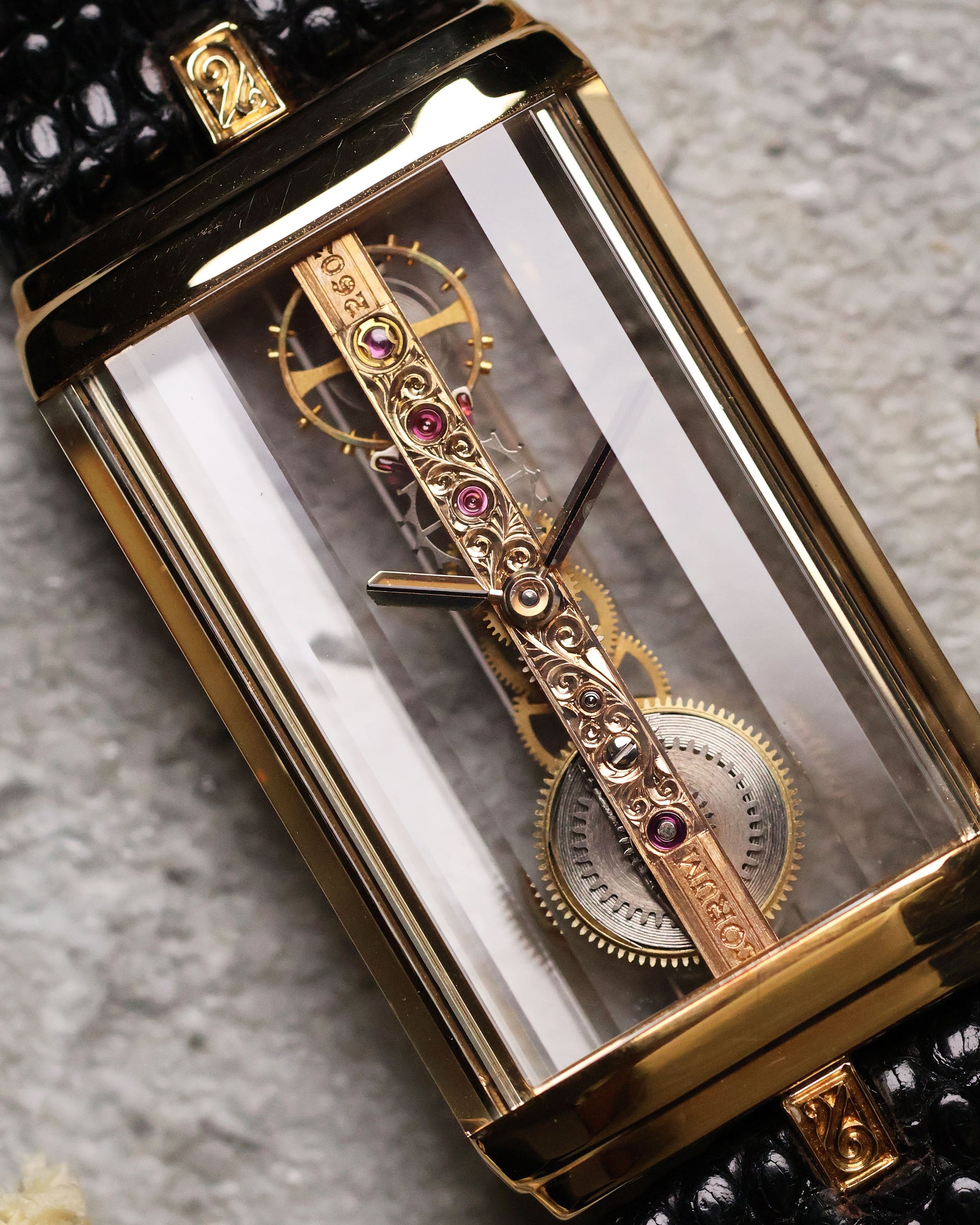 Close-up of the Corum Golden Bridge movement, highlighting the hand-engraved gold bridge with ruby jewels and “Corum” engraving, black hands, and exposed gears suspended within the sapphire case.