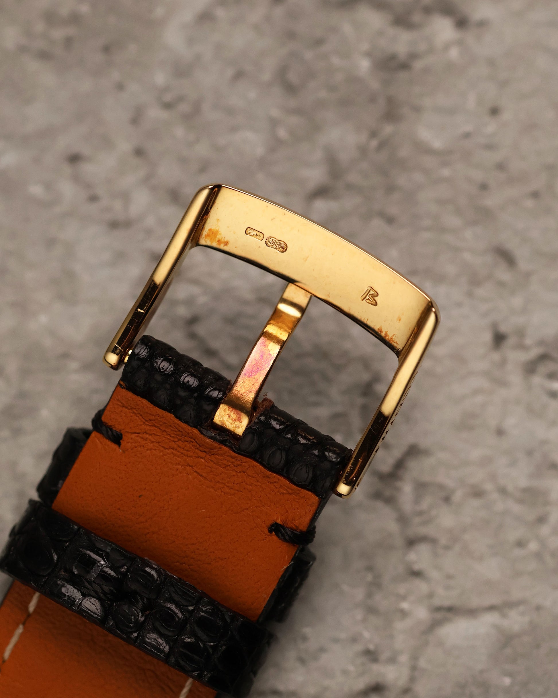 Underside view of the 18k yellow gold buckle, showing hallmarks and gold assay stamps, attached to a brown leather-lined strap.