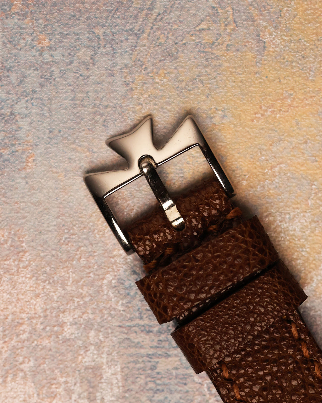 Vacheron Constantin platinum Maltese cross buckle on brown textured leather strap, emphasizing craftsmanship and design continuity.