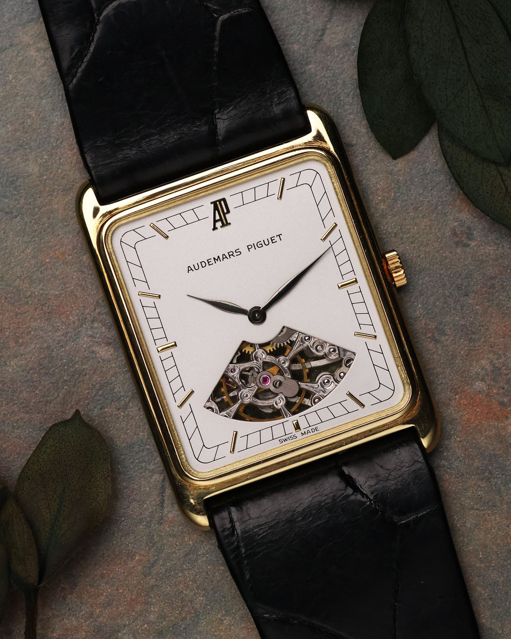 Flat lay of Audemars Piguet Skeleton Aperture Tank with leaves background, showcasing dial and skeleton aperture.