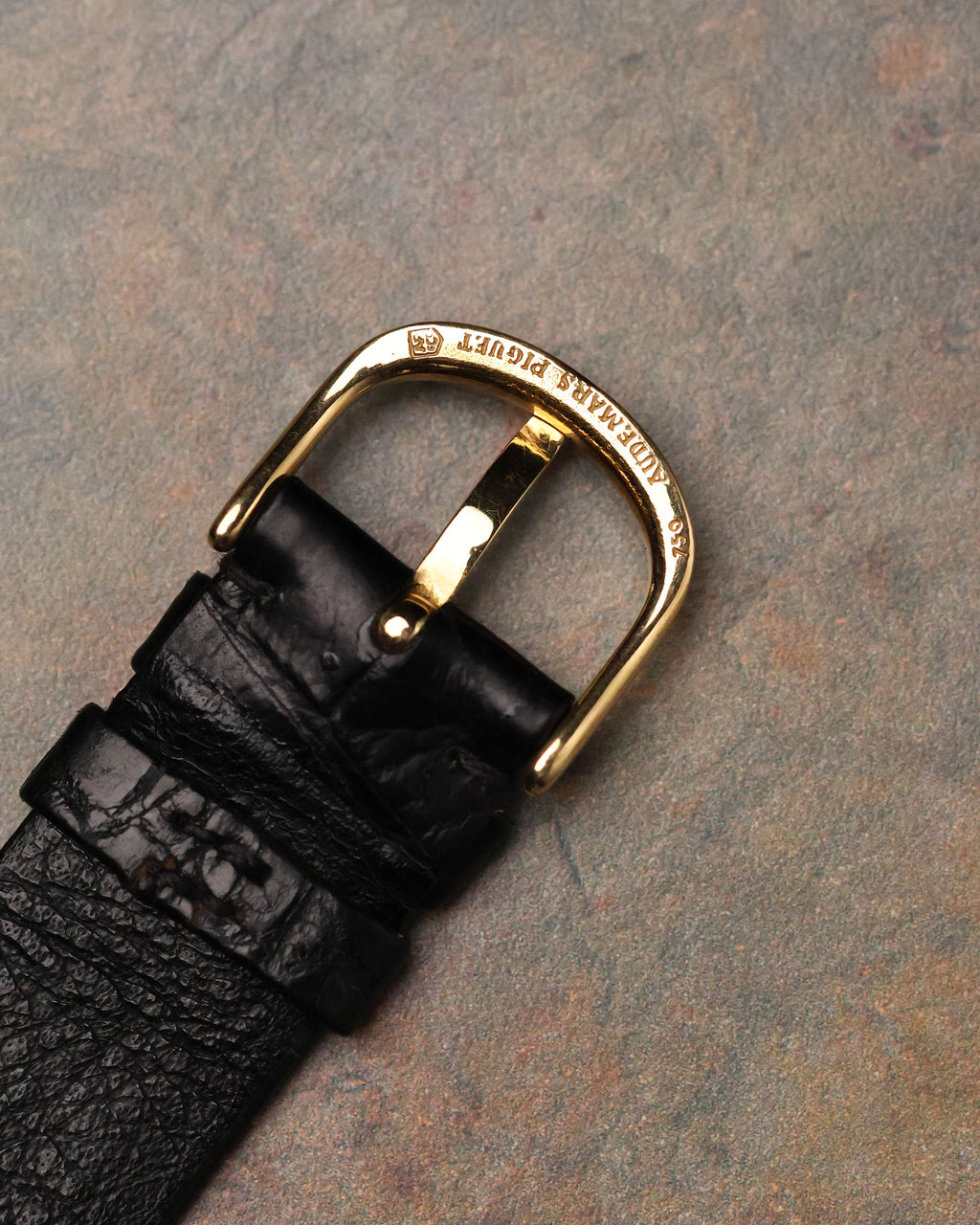 Close-up of original Audemars Piguet 18K gold buckle engraved with AP logo and hallmark.