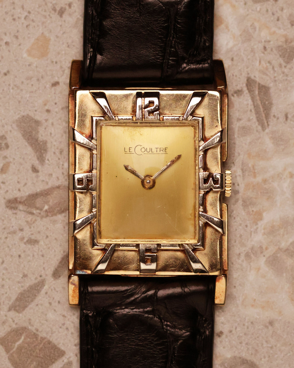 Close-up of a vintage LeCoultre 14K gold Art Deco tank watch showing the gold dial and distinctive raised silver numerals on the outer bezel.