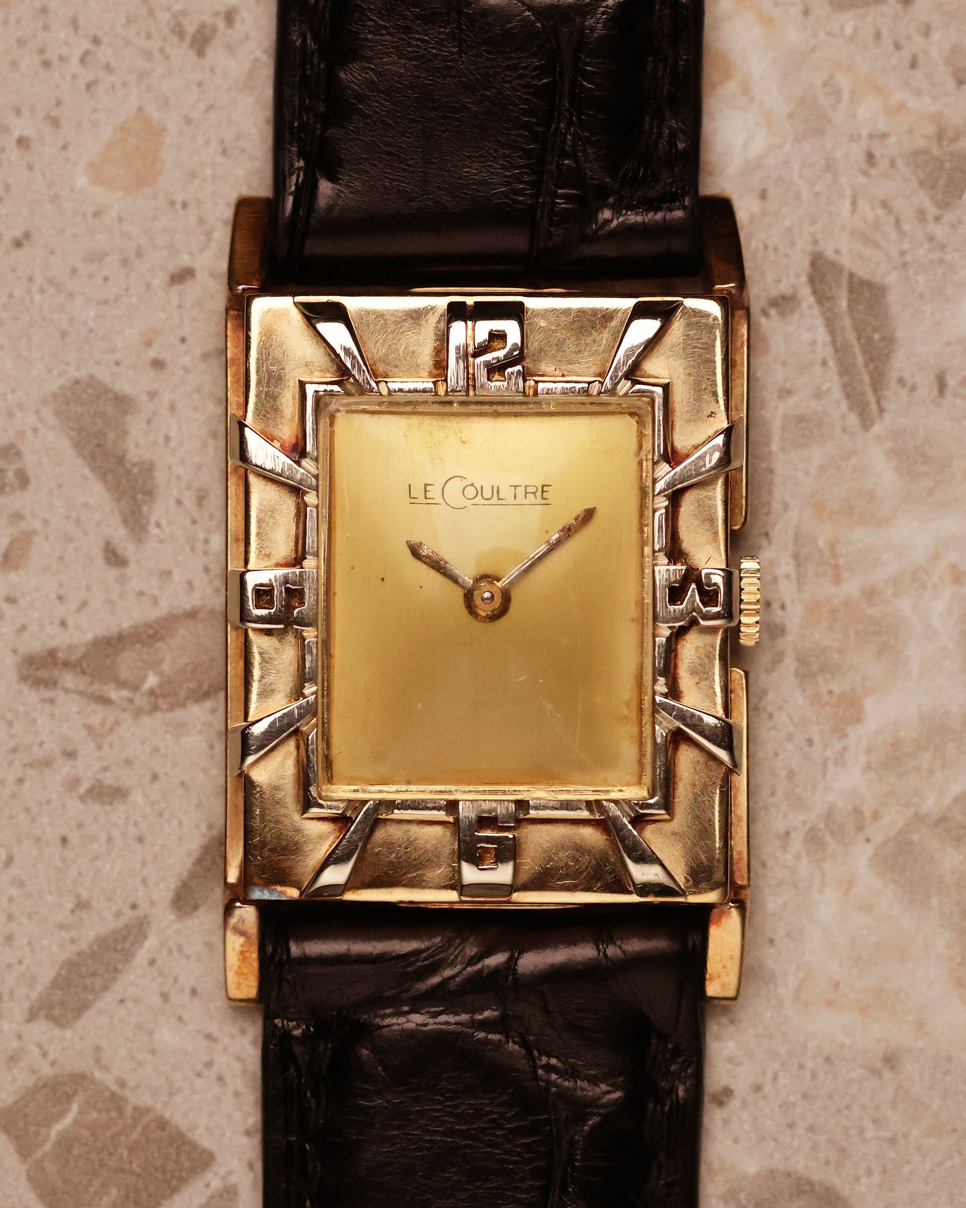 Close-up of a vintage LeCoultre 14K gold Art Deco tank watch showing the gold dial and distinctive raised silver numerals on the outer bezel.