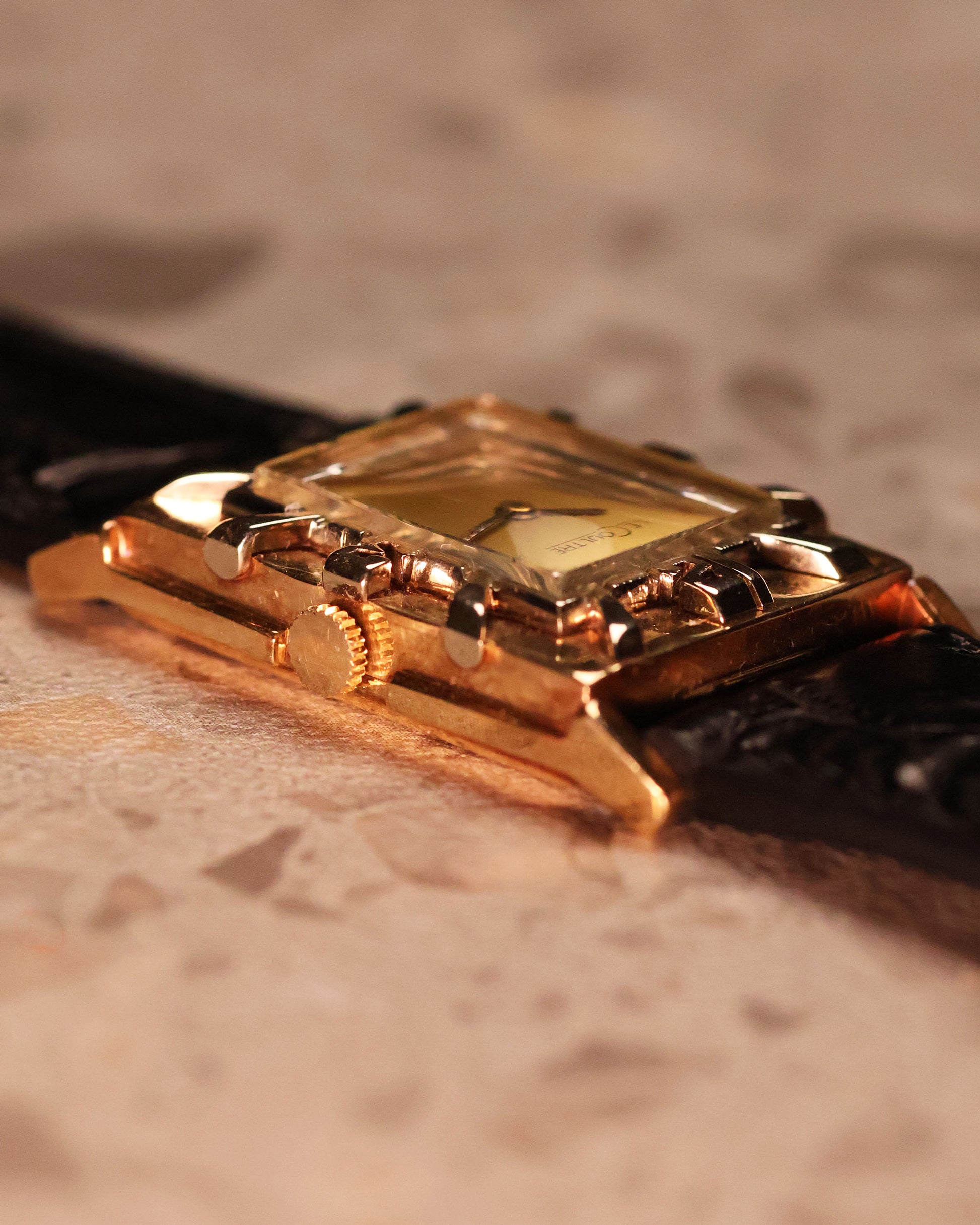 Angled close-up of the LeCoultre watch case showing the depth of the applied numerals on the gold bezel and smooth crystal curvature.