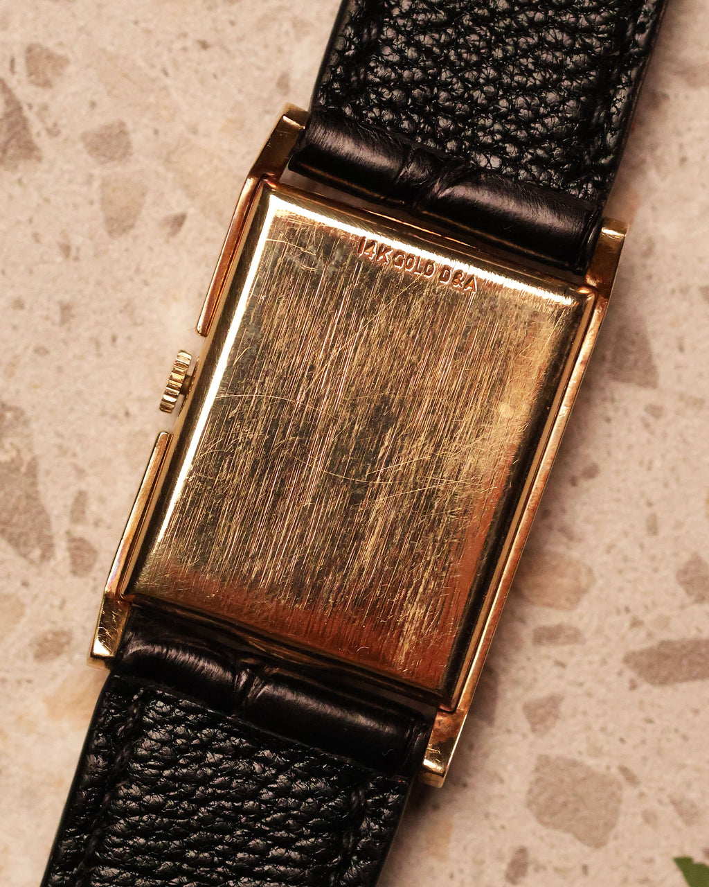 Back view of the LeCoultre vintage watch showing the solid 14K gold caseback stamped “14K GOLD D&A” and black leather strap.