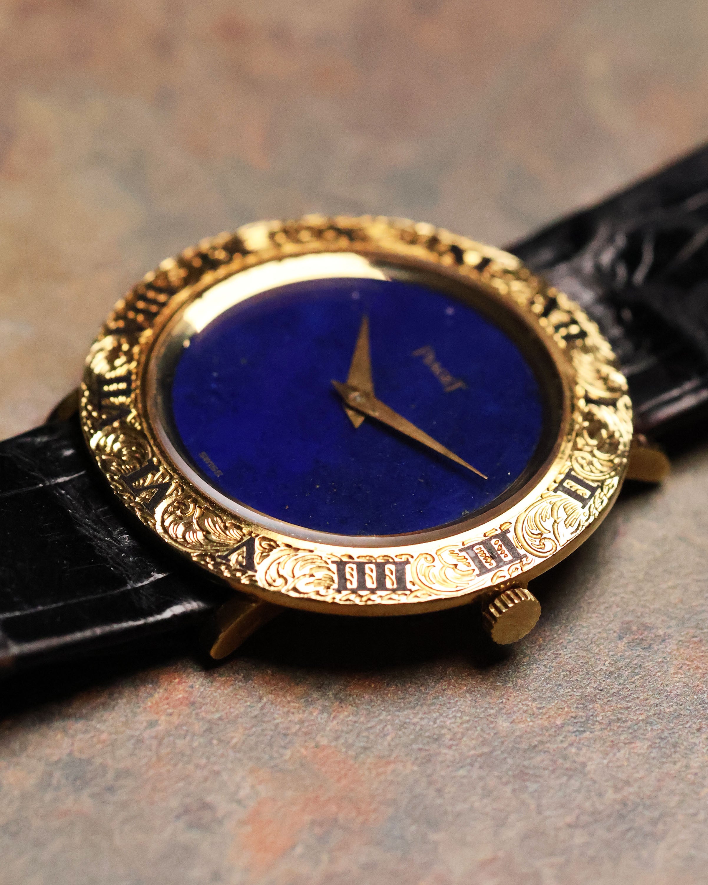 Low-angle shot of the Piaget 9118 showing the engraved Roman bezel and lapis stone dial, with the black leather strap partially visible.