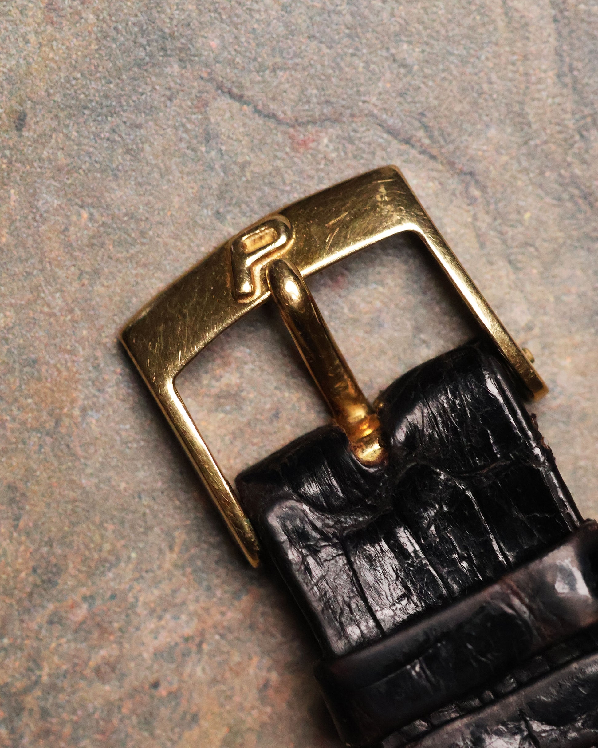 Close-up of the Piaget gold buckle with the raised “P” logo attached to a black leather strap.