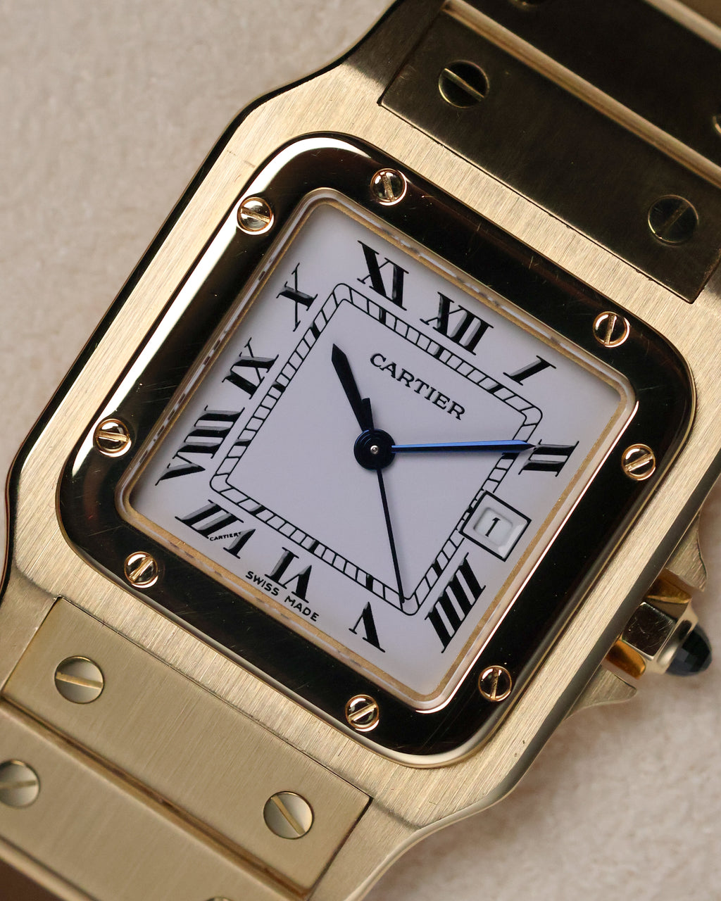 Macro close-up of the Cartier Santos Carrée dial, showing the white Roman-numeral face, chemin-de-fer minute track, blued hands, and date window at 3 o’clock.