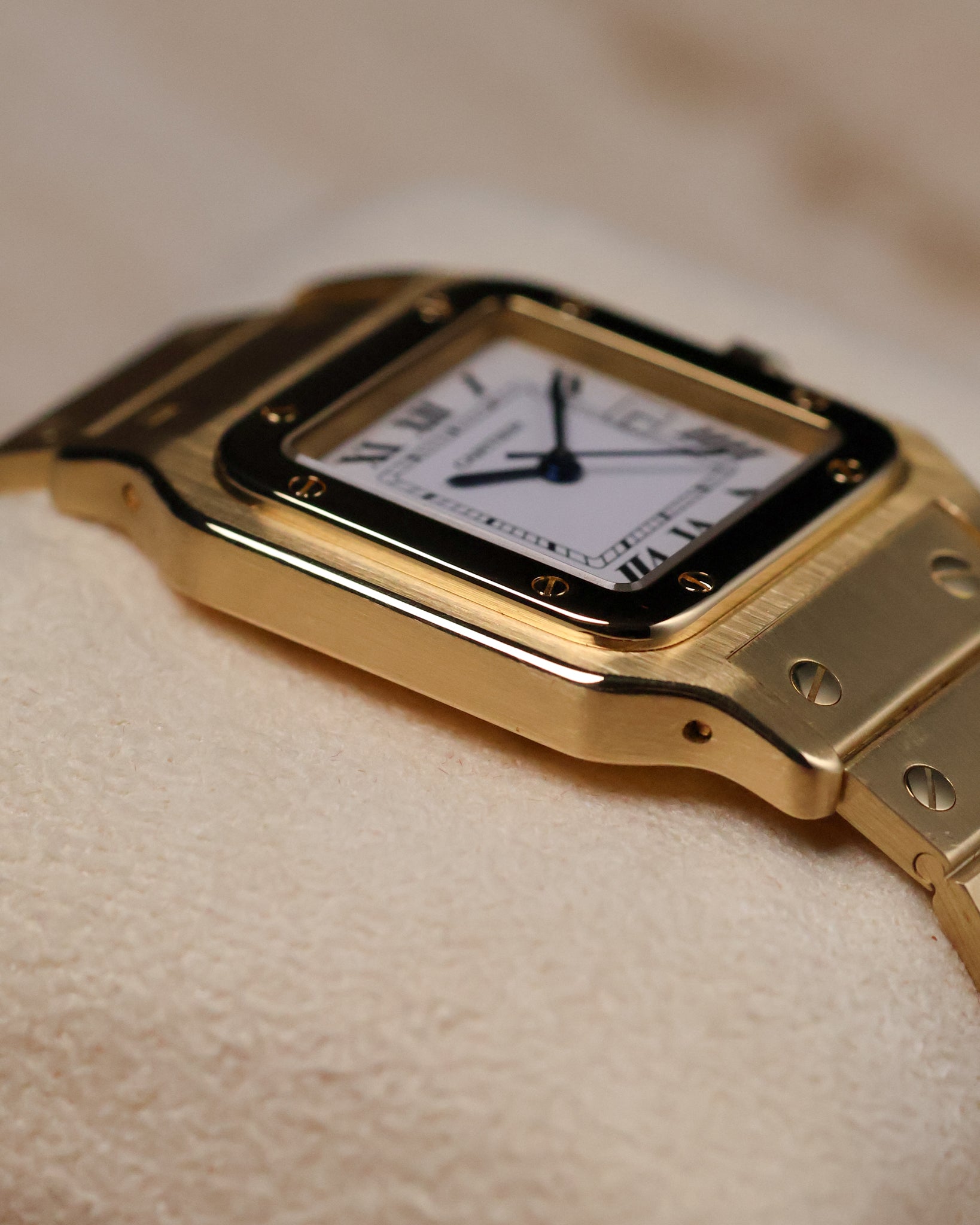 Low-angle macro shot of the Cartier Santos Carrée, emphasizing the contour of the gold case, polished bezel screws, and the edge of the bracelet links.