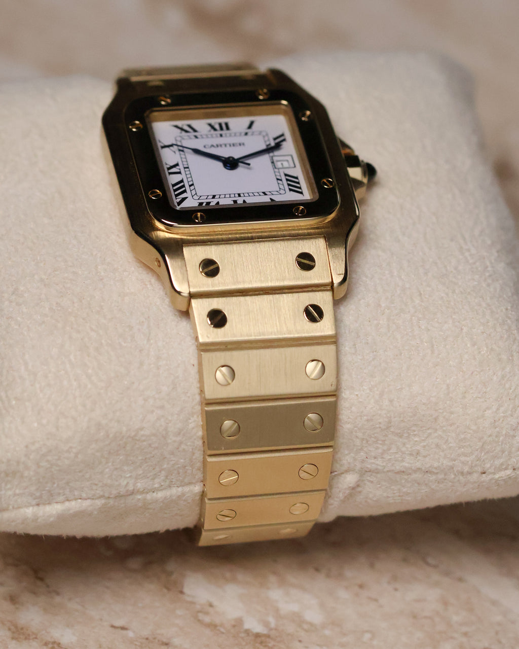 Close-up angled shot of a Cartier Santos Carrée Ref. 2960 in solid 18K yellow gold displayed on a cream cushion, showing the brushed gold bracelet with signature Santos screws and the white Roman-numeral dial.