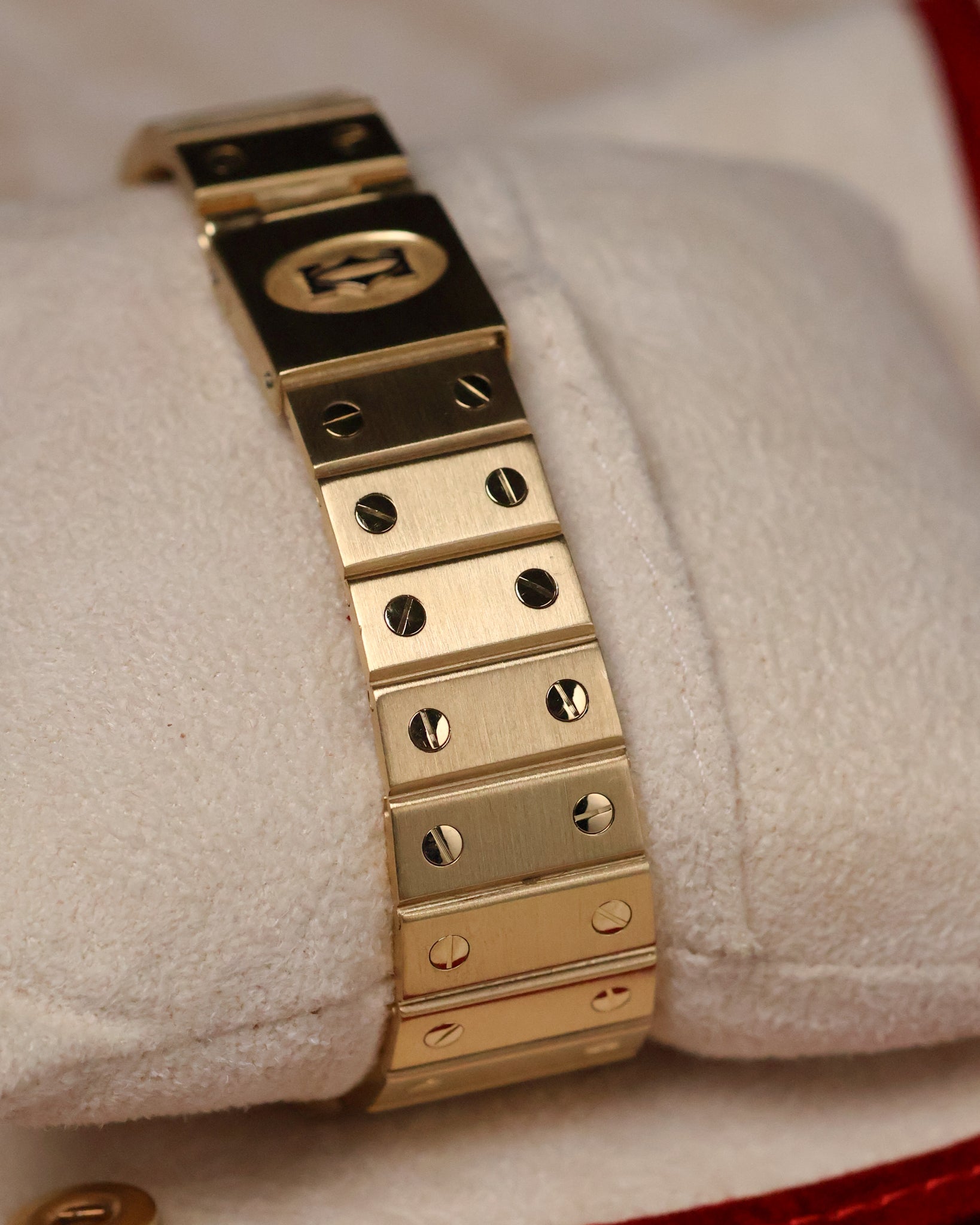 Angled shot of the Cartier Santos Carrée gold bracelet on a cushion, highlighting the uniform brushed links and screw-decoration pattern.