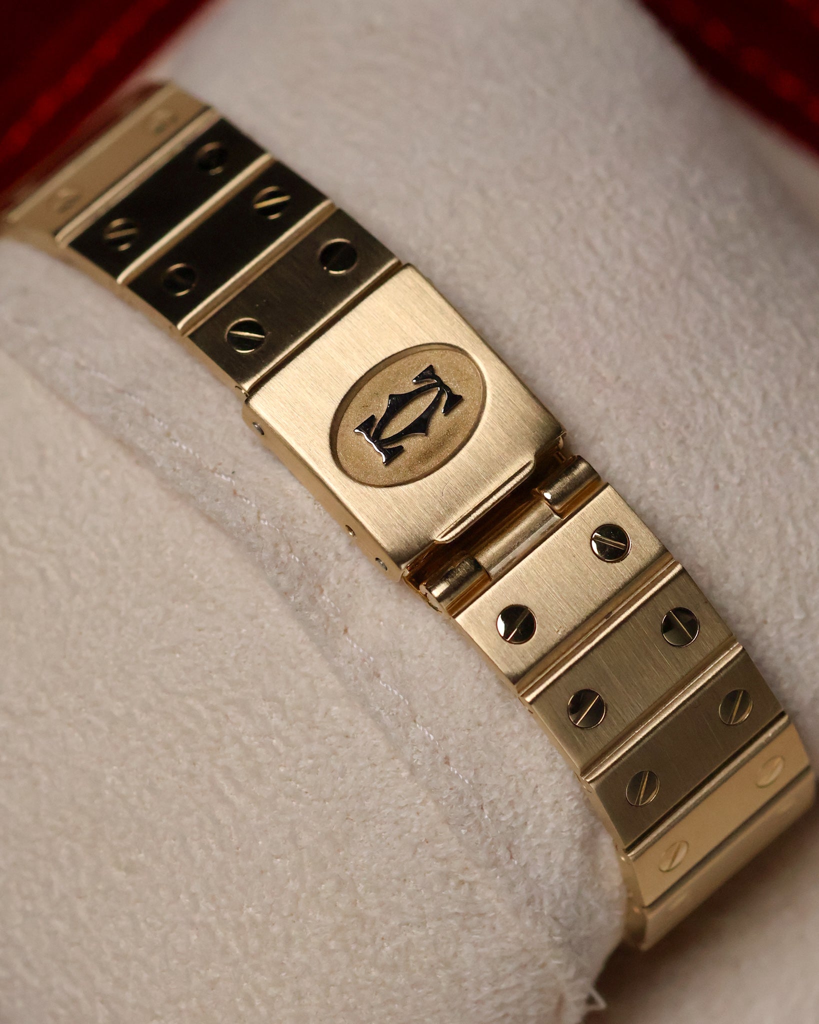 Top-down view of the Cartier Santos Carrée clasp, featuring the engraved Cartier emblem and brushed gold surfaces with polished screws.