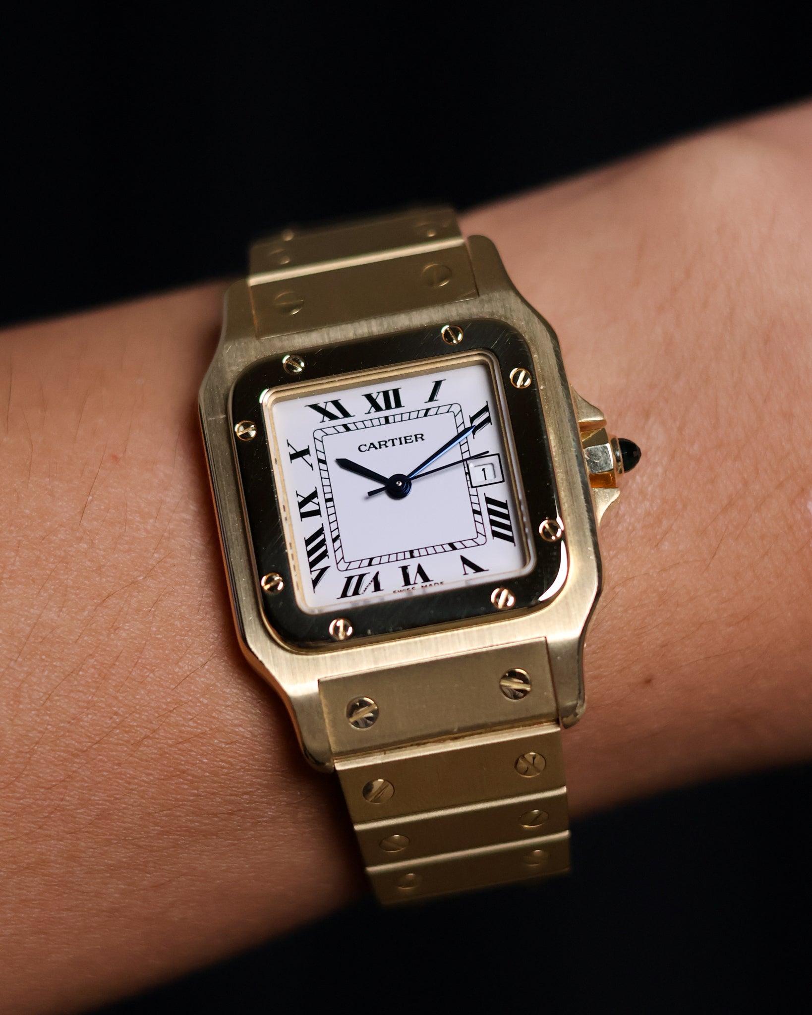 Wrist shot of the Cartier Santos Carrée Or Massif Ref. 2960 in solid 18K yellow gold, showing the watch worn on the wrist with the bright white Roman dial and blue cabochon crown.