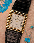 Top-down view of a Rolex Cellini Ref. 4015 in solid 18K yellow gold, showing the asymmetric ribbed case, Roman numeral dial, and black leather strap with blue floral accents.