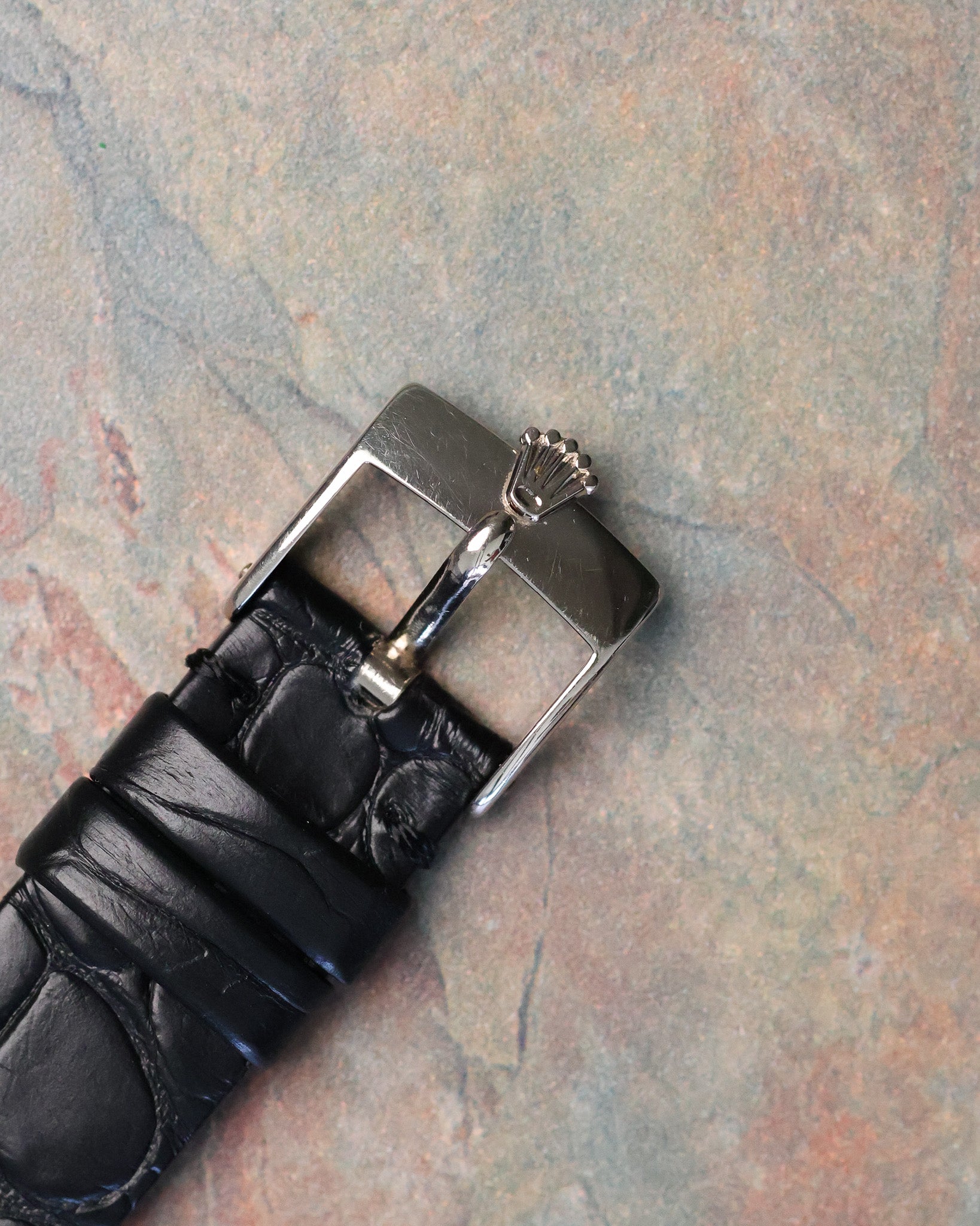 Original Rolex 18K white gold tang buckle with embossed crown logo attached to black leather strap.