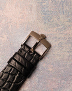 Original 18K white gold Rolex pin buckle attached to black leather strap, viewed from the top.