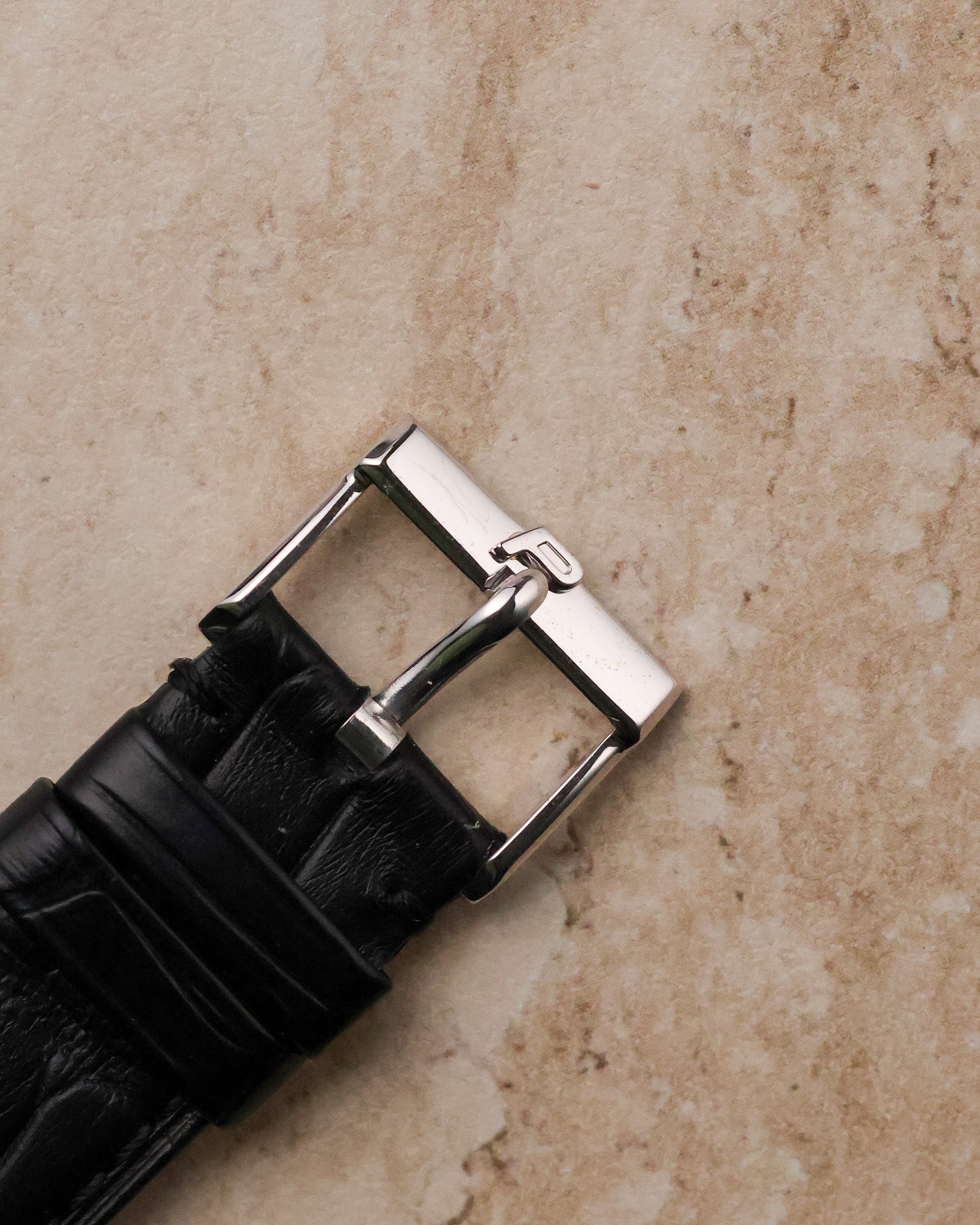 Original 18K white gold Piaget tang buckle attached to black leather strap, top view detail.