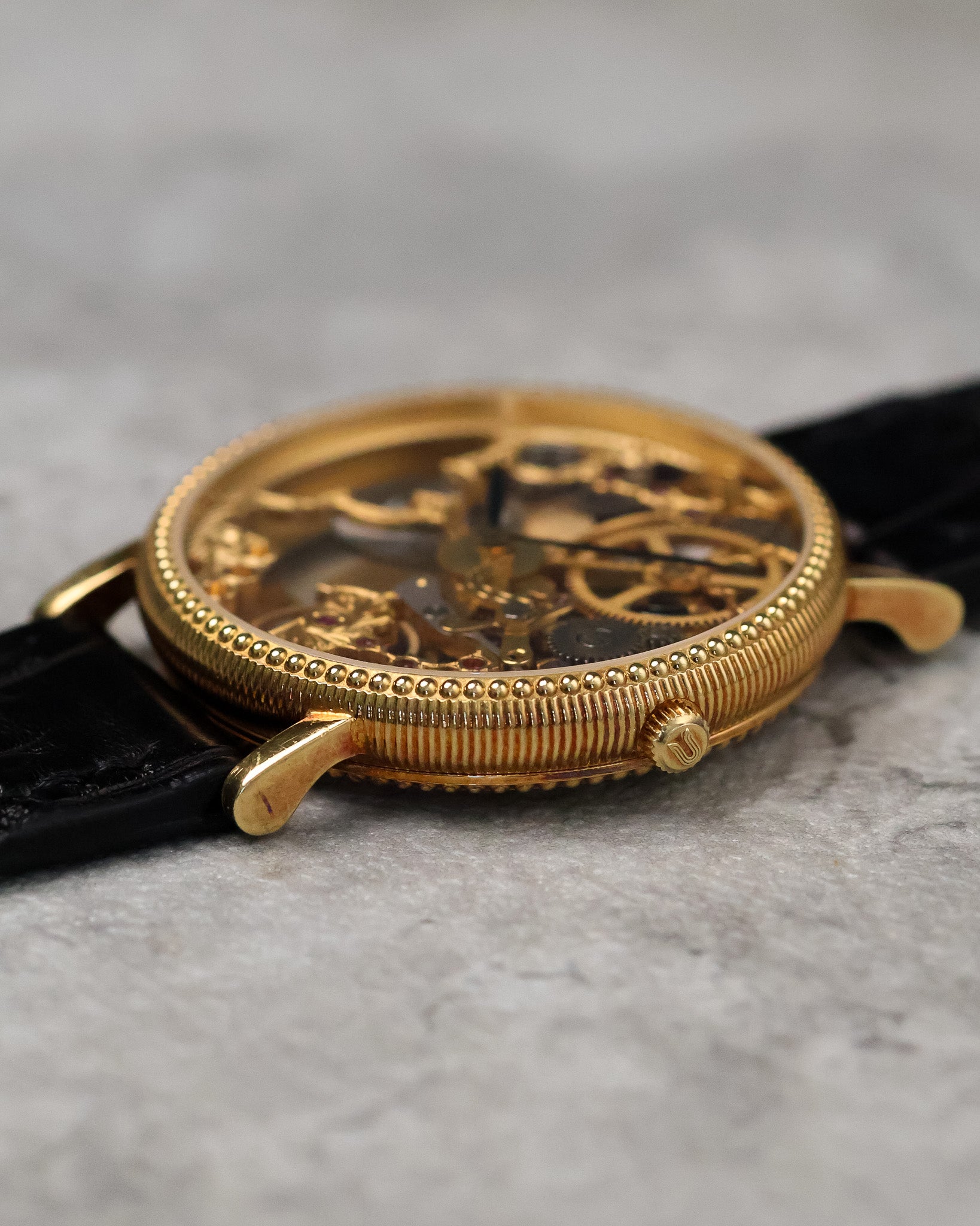 Side angle showing the fluted caseband, coin-edge bezel, and signed crown on the Universal Genève skeleton watch.