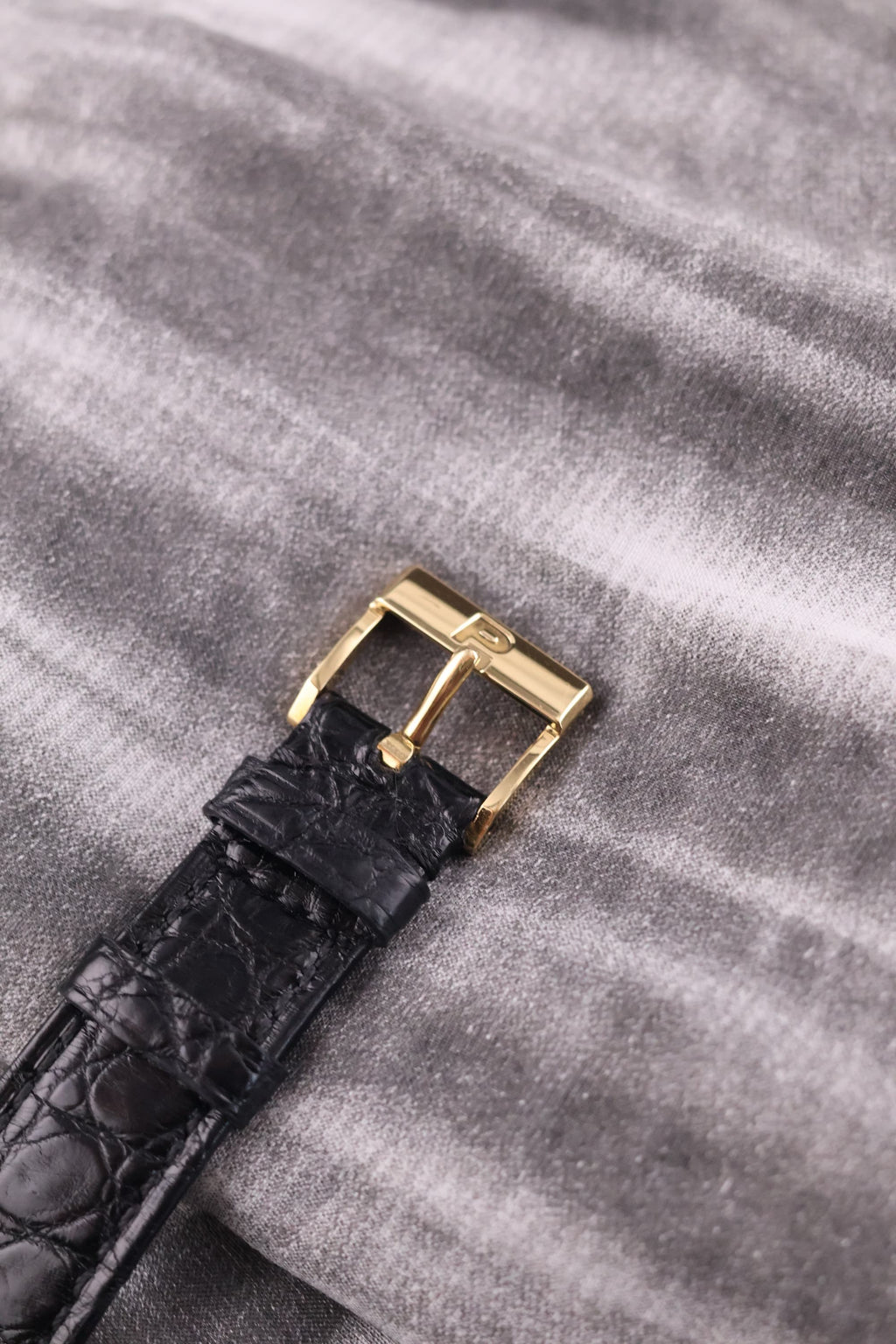 Detail of the original Piaget-signed 18K yellow gold buckle, attached to a black leather strap.