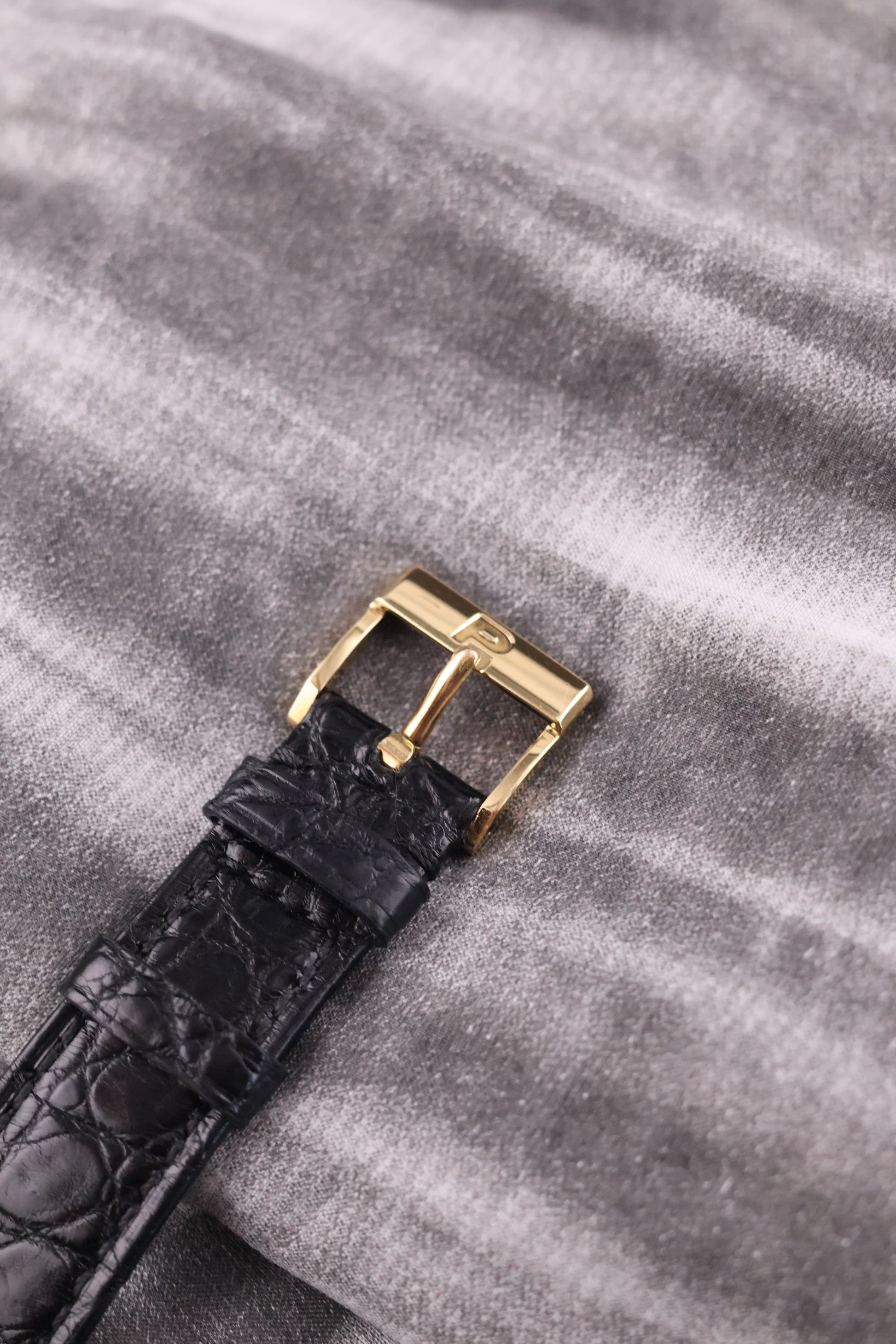 Detail of the original Piaget-signed 18K yellow gold buckle, attached to a black leather strap.